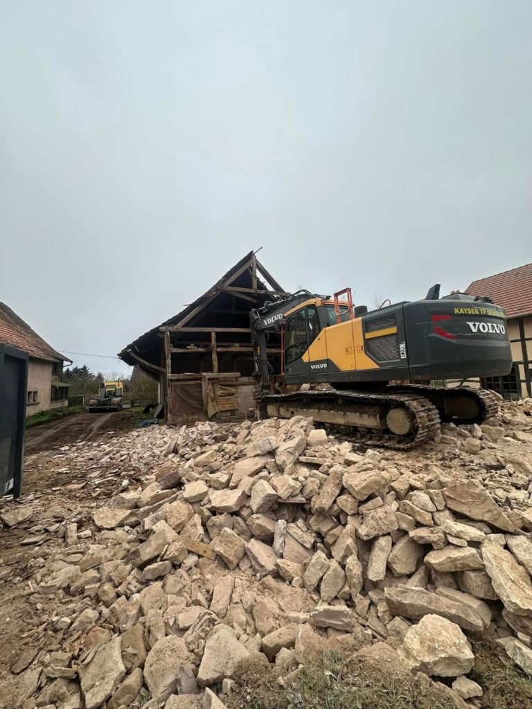 Pelle Volvo et tas de gravats pendant la démolition de la maison avec grange à Fontaine